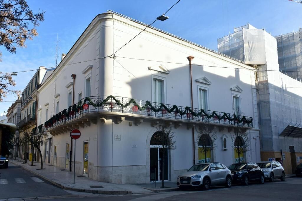 A white building with a balcony, parked cars, and a no entry sign.