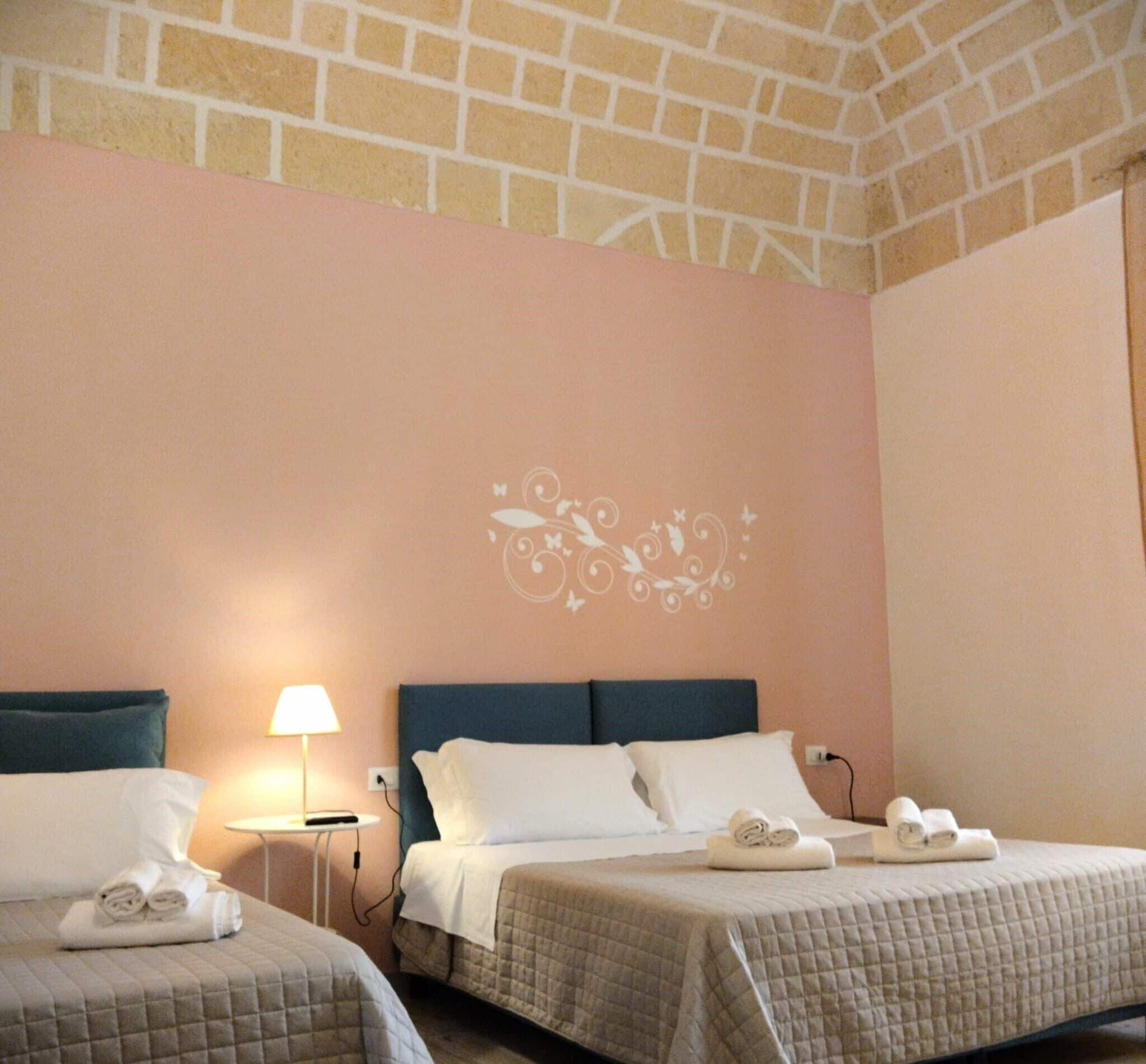 A hotel room with two beds, a decorative wall mural, a lamp, and neatly folded towels on each bed.