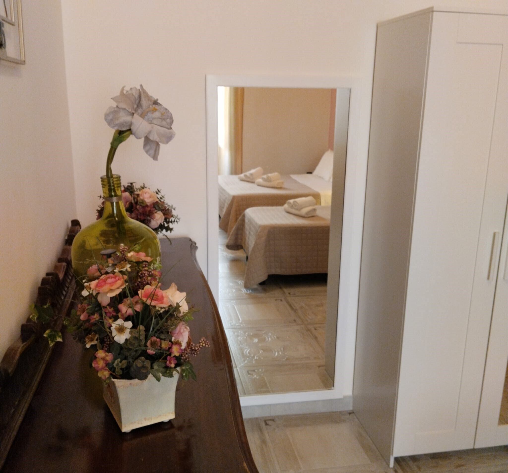 Una habitación de hotel con dos camas, un armario y un jarrón decorativo con flores sobre una mesa.