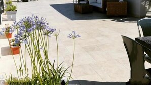 Una terraza en la azotea con mobiliario exterior, plantas en macetas y vistas a edificios al fondo.