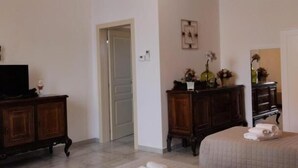 Una habitación de hotel con techo de ladrillo, dos camas, un televisor, un aparador y una puerta que da a otra habitación.