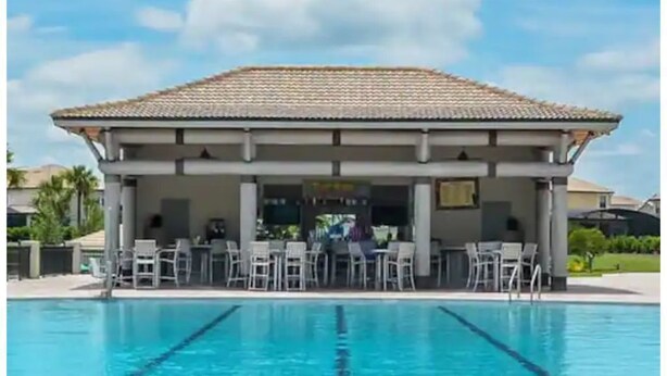 A swimming pool with a covered area and chairs, surrounded by a fence. - Champions Family Home - Near Disney (Davenport)