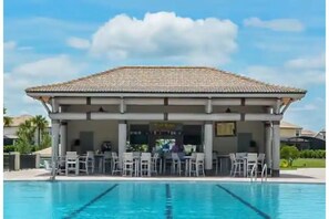 Ein Schwimmbecken mit überdachtem Bereich und Liegestühlen, umzäunt.