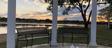 A park with a chessboard and benches under white columns, overlooking a lake.