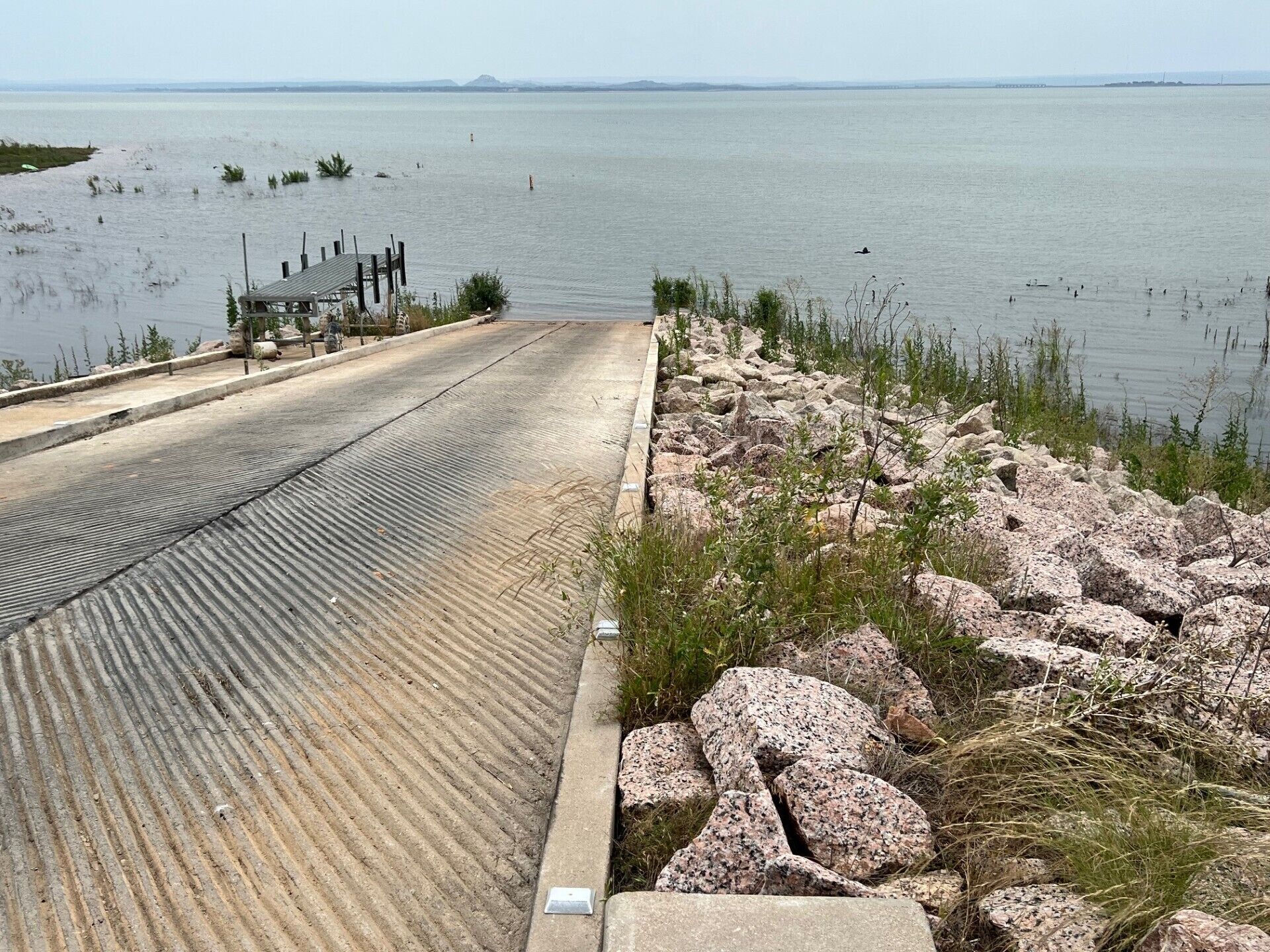 A concrete viewing platform with a metal railing overlooking a calm body of water.
