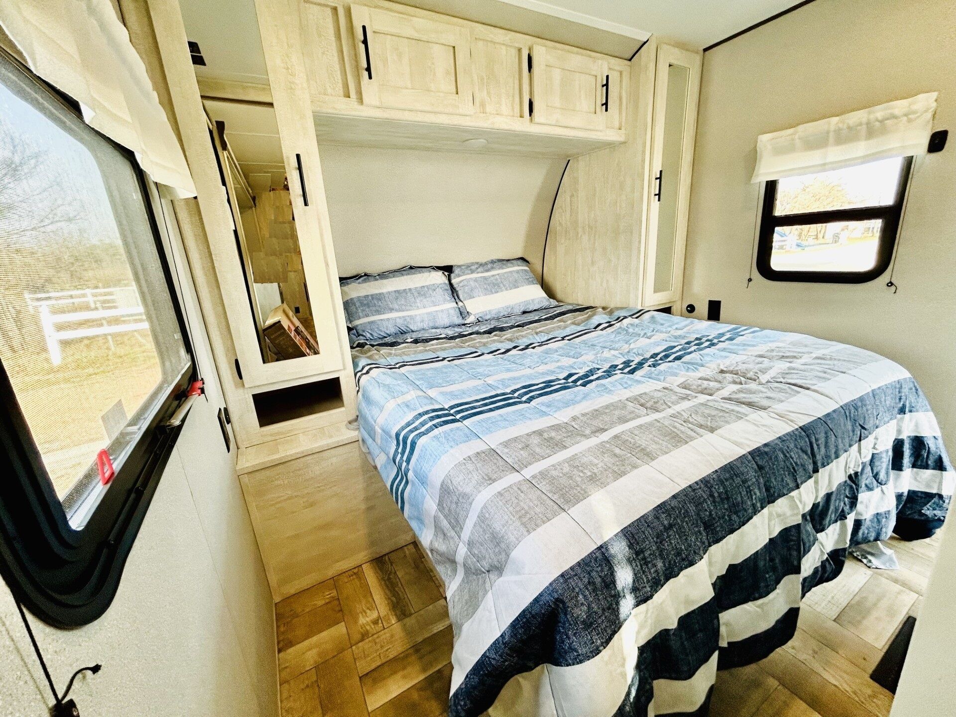 A compact RV bedroom with a bed, a window, and a small window with a view.