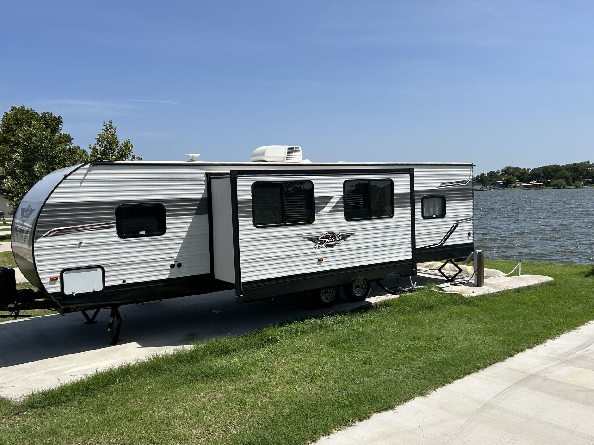 Un camping-car argenté, doté d’une porte coulissante, d’une petite fenêtre et d’une lanterne de toit blanche, était stationné près d’une étendue d’eau.