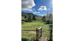 A rural landscape with a wooden gate, a clear sky, and a hilly backdrop. - Gite Herisson, Nid Pour Amoureux Dans la Nature (Avène)