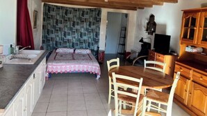 A compact kitchen with a wooden dining table and chairs, a bed with a patterned bedspread, and a tiled backsplash. - Gite Herisson, Nid Pour Amoureux Dans la Nature (Avène)