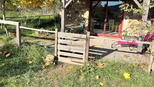 A rustic stone building with a wooden gate, a covered outdoor seating area, and a view of a hillside. - Gite Herisson, Nid Pour Amoureux Dans la Nature (Avène)