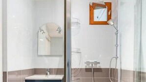 Un bany modern amb dutxa envidriada, un lavabo amb mirall i un armari blau.