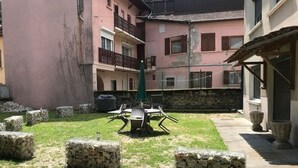 Un pati amb taula i cadires, jardineres de pedra i un edifici amb balcons i finestres.