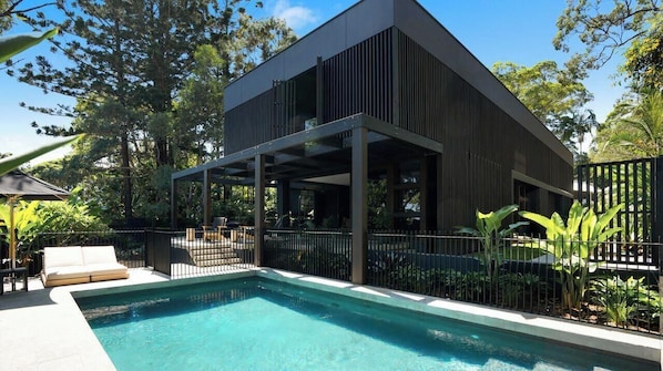 A modern building with a pool, outdoor seating, and a covered area.