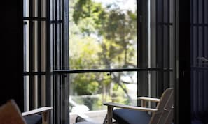 A room with a view of trees through a window, a chair, and a table.