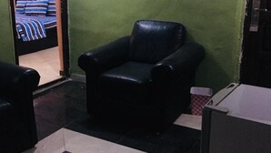 Une pièce avec un fauteuil en cuir noir, une petite table et un sol carrelé dont le motif ressemble au marbre.
