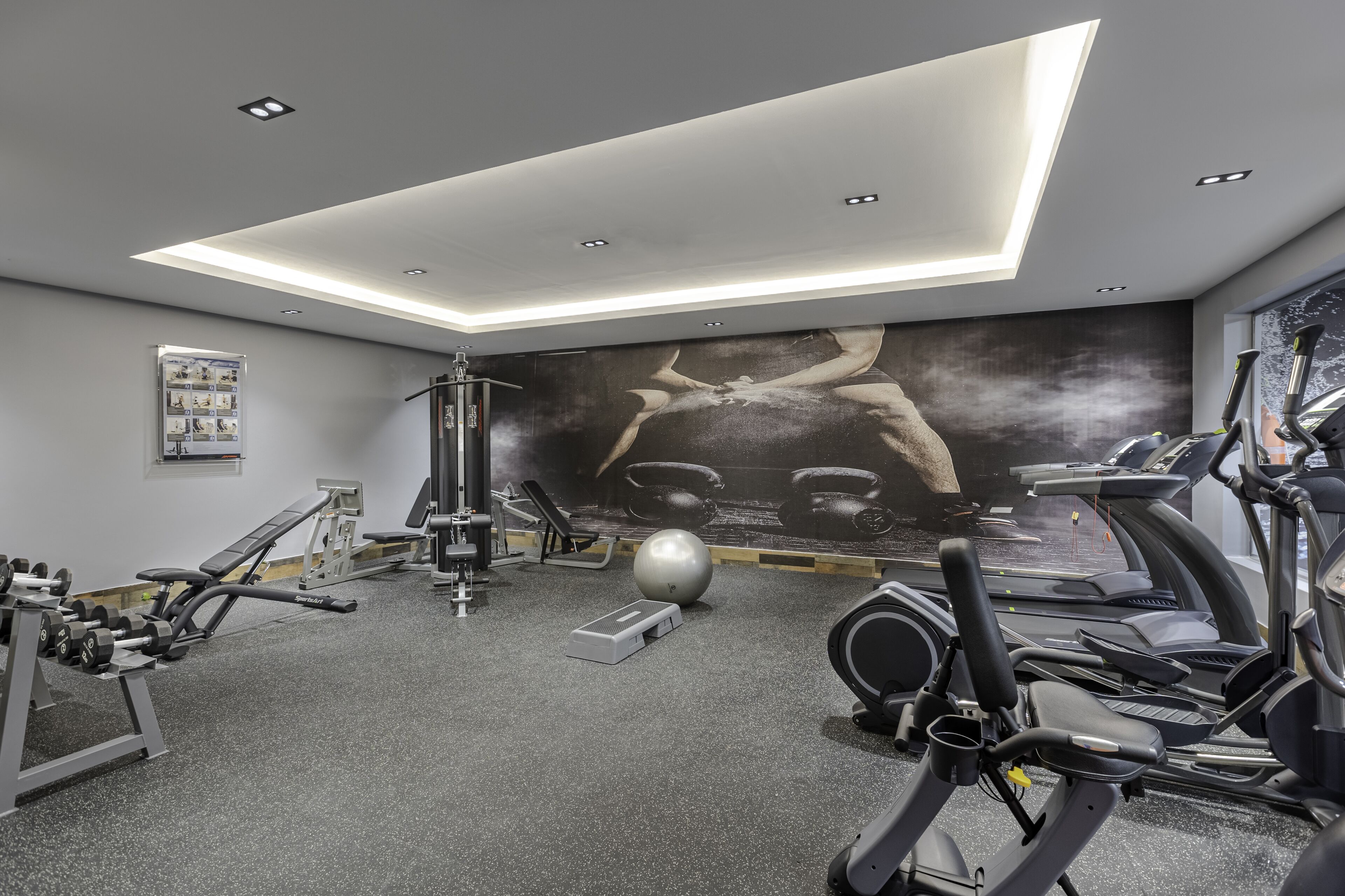 A modern gym with various exercise equipment, a large wall mural, and a skylight.