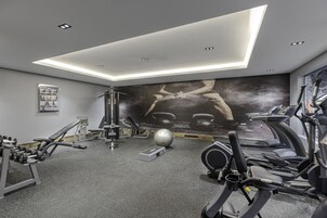 A modern gym with various exercise equipment, a large wall mural, and a skylight.