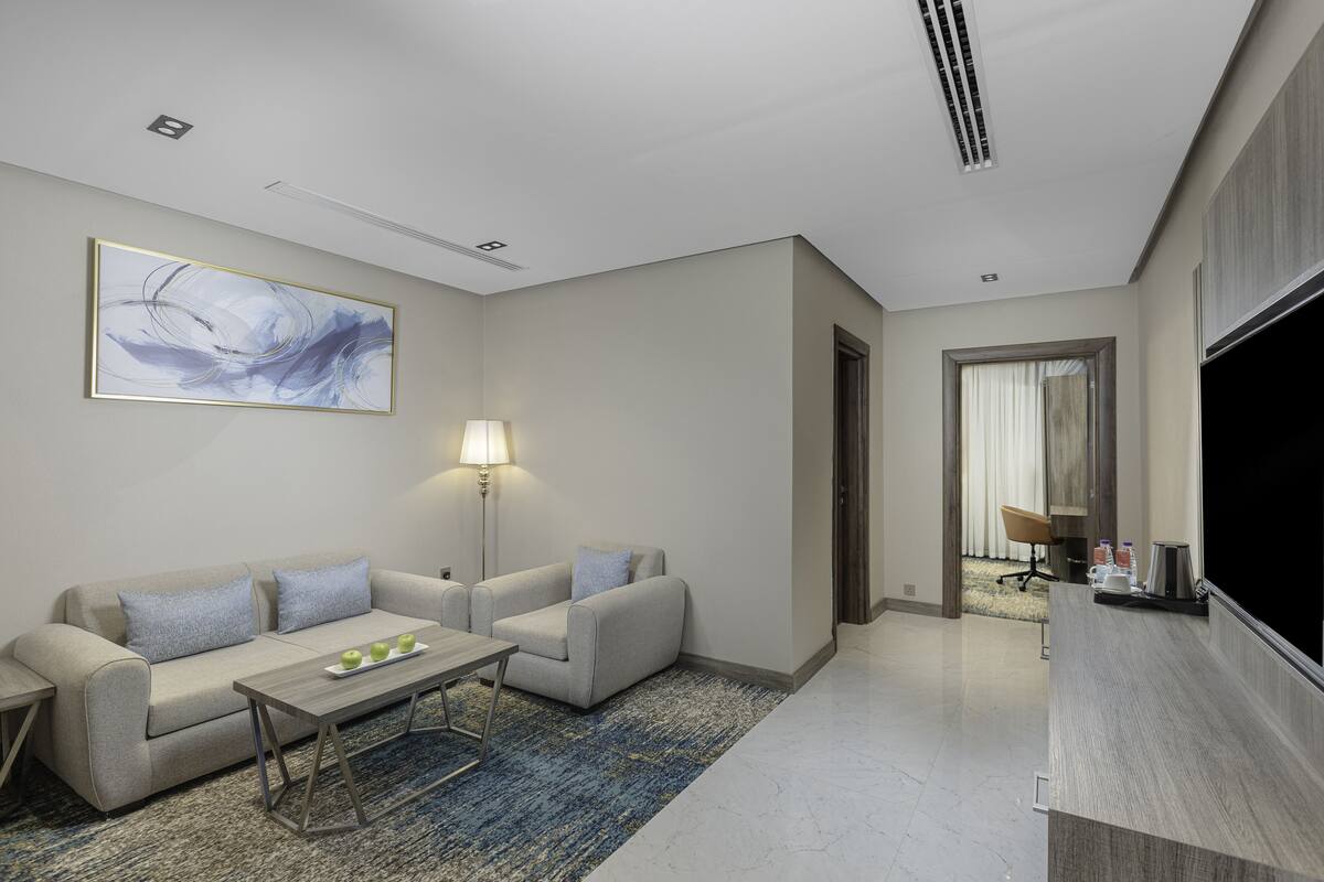 A modern hotel room with a sofa set, a coffee table, a flat-screen TV, and a painting on the wall.