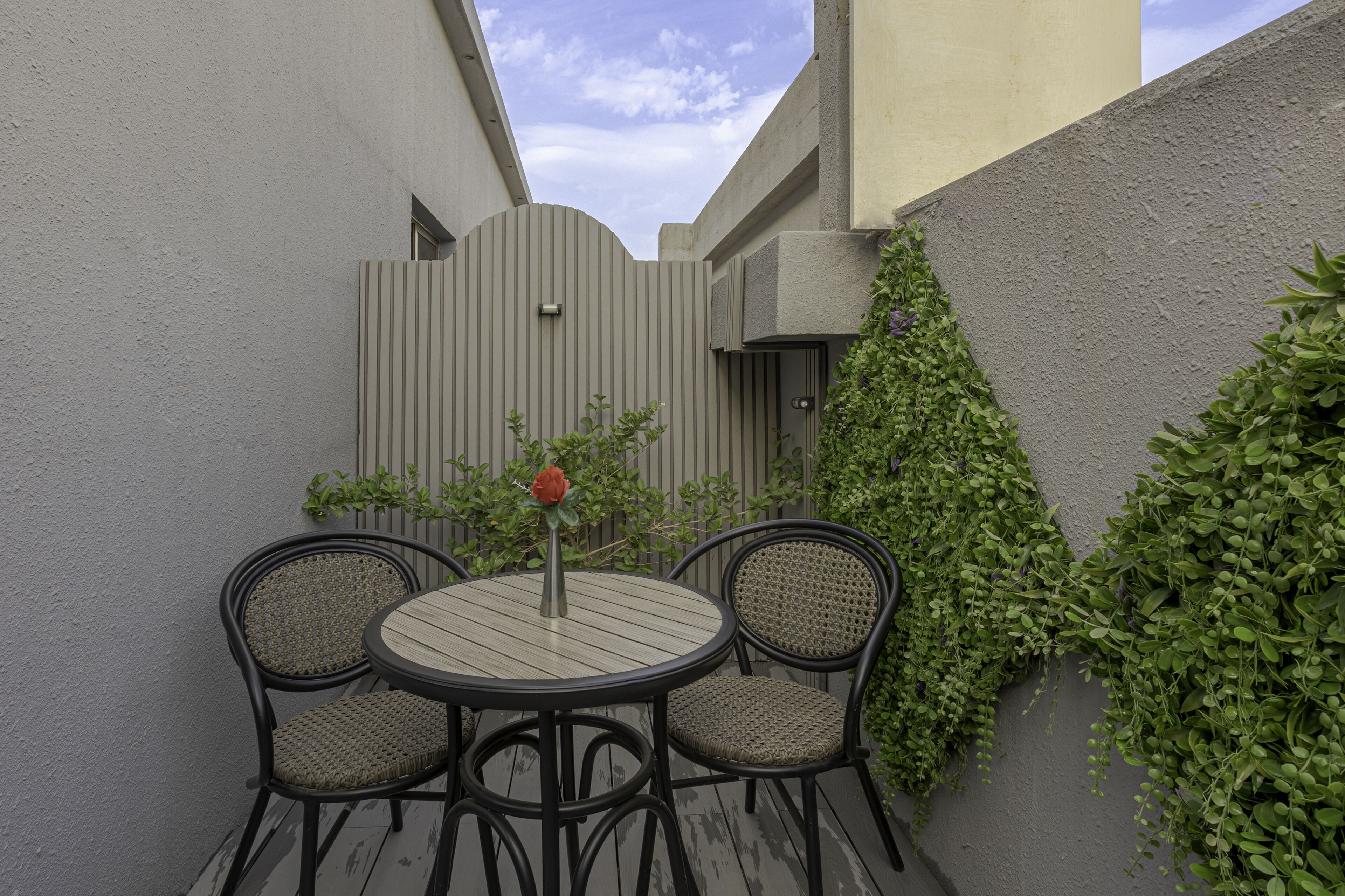 A patio with two wicker chairs and a table, surrounded by a grey wall with climbing plants.