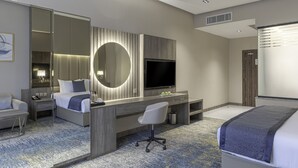 A modern hotel room with a large bed, a desk with a computer, a TV, and a large mirror. - Seven Gardens Hotel (Riyadh)