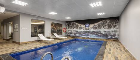 An indoor swimming pool with clear water, a lifeguard stand, and a mural of a swimmer on the wall.