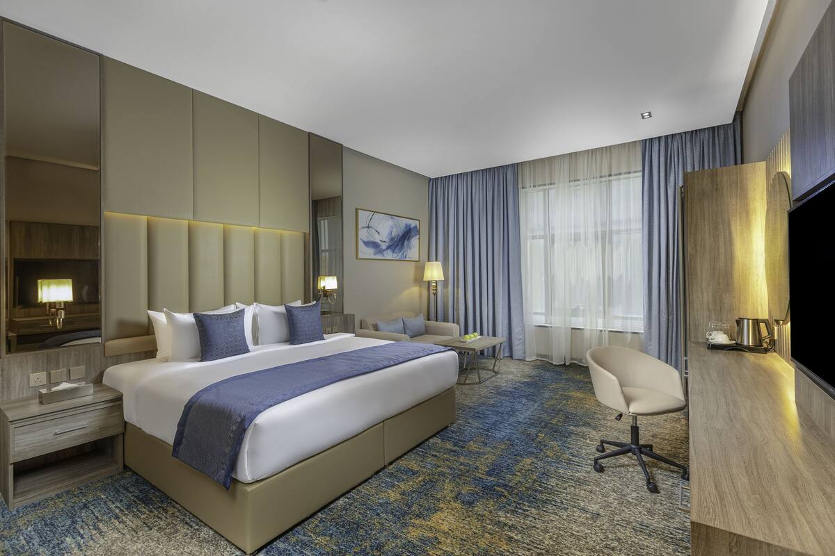 A hotel room with a large bed, a desk, a chair, a TV, and a window with curtains.
