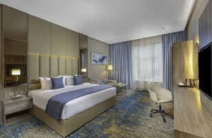 A hotel room with a large bed, a desk, a chair, a TV, and a window with curtains.