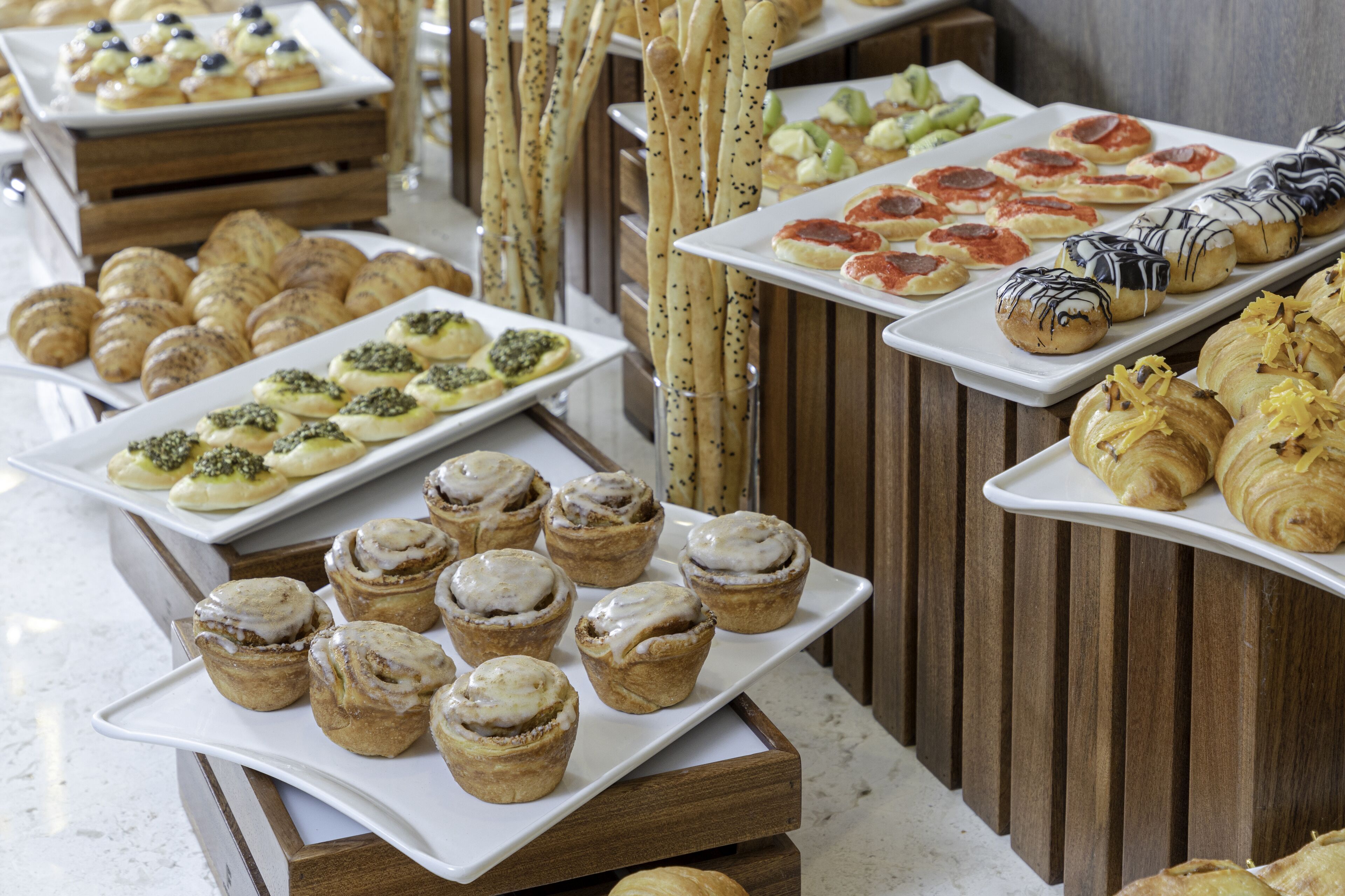 A buffet with various pastries and desserts arranged on white plates and wooden stands.