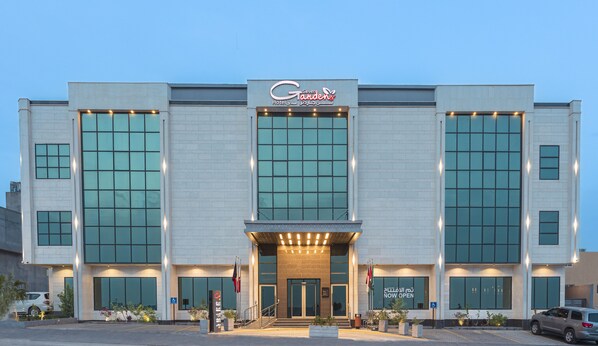 A hotel with a modern facade, large windows, and a sign indicating it is now open. - Seven Gardens Hotel (Riyadh)