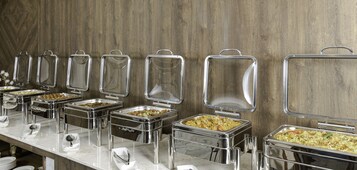Una barra de buffet con varios recipientes de comida y utensilios para servir.