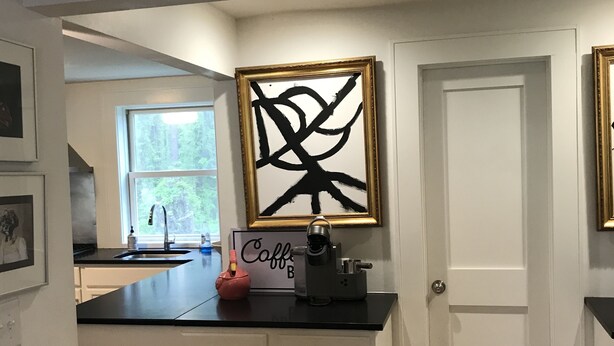 A kitchen with white cabinets, a black countertop, and a coffee machine. There is a framed abstract artwork on the wall and a sign that says "Coffee Bar". - Renovated historic home! (Chapel Hill)