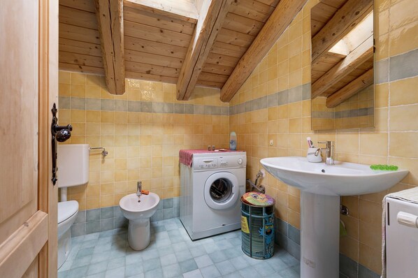 Un baño pequeño equipado con lavadora, inodoro, lavamanos y un cubo de basura.