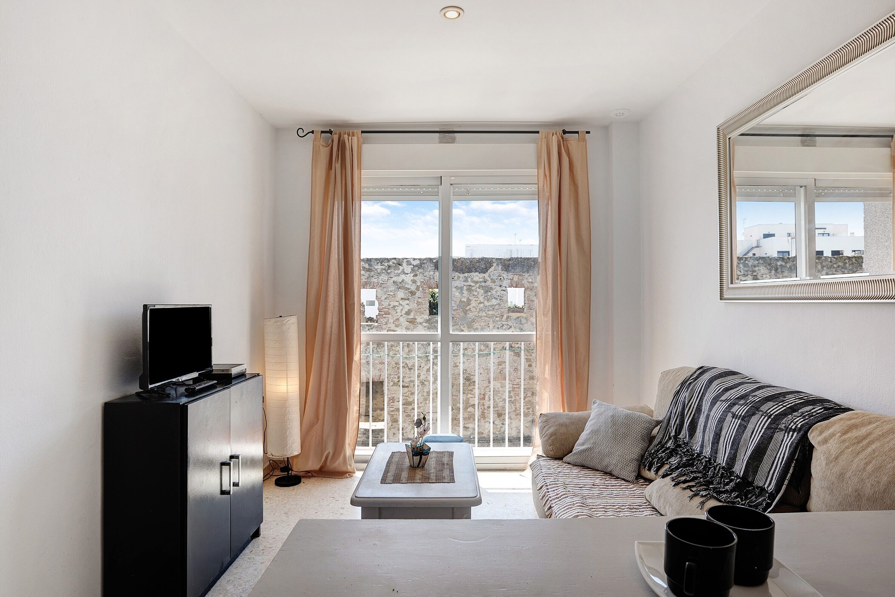 Een moderne woonkamer met een bank, een salontafel, een televisie op een kast en een balkon met gordijnen.