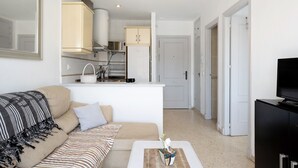 Una sala de estar con sofá, una mesa de centro, un mueble para televisión y una zona de cocina al fondo.