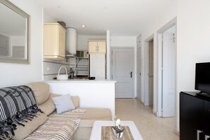 A living room with a sofa, a coffee table, a TV stand, and a kitchen area in the background.