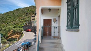 A staircase leading to a building entrance with a metal gate, a red car parked on the street, and a hillside in the background. - Holiday Home 'Casa Luci' with Sea View, Private Terrace and Wi-Fi (Levanto)