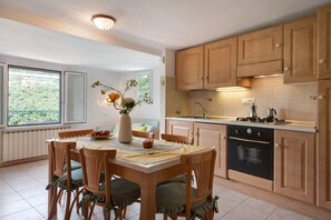 A kitchen with wooden cabinets, a dining table with chairs, a vase with flowers, and a view through the window.