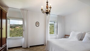 A bedroom with a bed, a chandelier, a window with curtains, and a view of greenery outside. - Holiday Home 'Casa Luci' with Sea View, Private Terrace and Wi-Fi (Levanto)