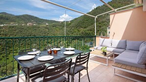 A balcony with a table set for dining, a sofa, and a view of a green hillside. - Holiday Home 'Casa Luci' with Sea View, Private Terrace and Wi-Fi (Levanto)