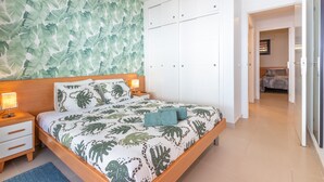 Une chambre à coucher comprenant un lit, des tables de chevet, une armoire et un mur orné d’un motif de feuilles.