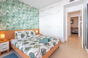 Une chambre à coucher comprenant un lit, des tables de chevet, une armoire et un mur orné d’un motif de feuilles.