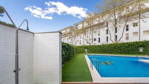 Un espace piscine avec une terrasse en bois, une petite pelouse et un bâtiment blanc doté de balcons.