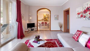 Una sala de estar con un sofá, una mesa de centro con flores, un televisor y un rincón de comedor visible a través de un arco.