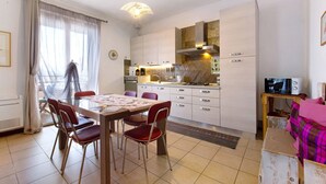 Una cocina moderna con armarios blancos, una mesa de comedor con sillas y un televisor sobre un mueble de madera.