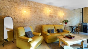 Una sala de estar con dos sofás amarillos, una mesa de centro de madera, un muro de piedra y una lámpara colgante.