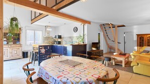 Amplia sala de estar con una mesa de comedor, sillas, un sofá, una cocina al fondo y una escalera.