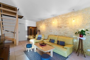 A living room with a sofa, coffee table, and a small stool. There is a wooden ladder, a potted plant, and a stone wall. - Logement Pascal – Bright, Air-Conditioned House with Pool Table (Villeneuve-sur-Lot)