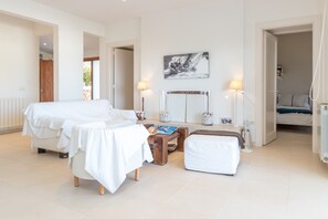 A spacious bedroom with two beds, a bedside table, a reading area, and a large window.