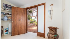 Puerta de madera abierta que da a un espacio exterior con pared de piedra y follaje.