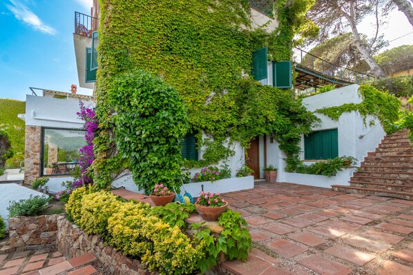 Un bâtiment à l’extérieur blanc, avec des volets verts et un escalier en pierre menant à une porte.